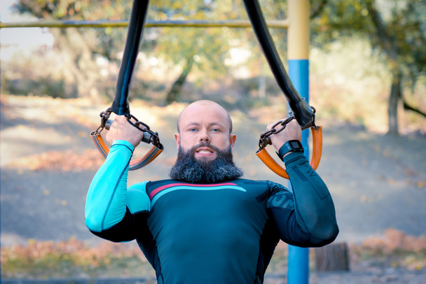М'язистий бородатий чоловік тренується з ремінцями
 - Фото, зображення