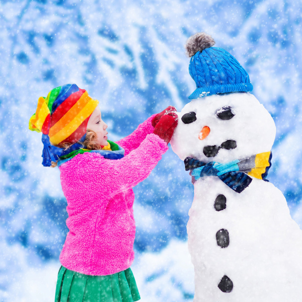 Petite fille construisant un bonhomme de neige en hiver
 - Photo, image