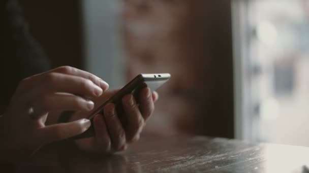 Close-up van de handen. Vrouw met behulp van haar smartphon touchscreen apparaat in loft café 4k - Video