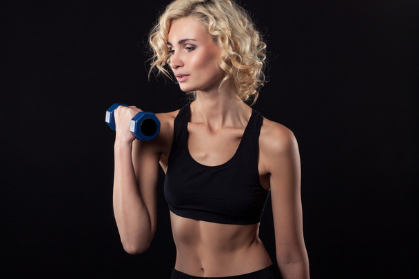 Torso of a young fit woman lifting dumbbells on dark background - Photo, Image