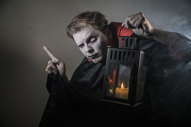 upiorny halloween Wampir wskazujący palec z latarnią na sobie czarna peleryna na ciemnym tle - Zdjęcie, obraz