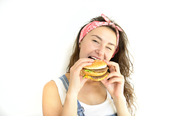 όμορφο κορίτσι hipster με όρεξη δαγκώματα burger. Μοντέλο σε λευκό φόντο - Φωτογραφία, εικόνα