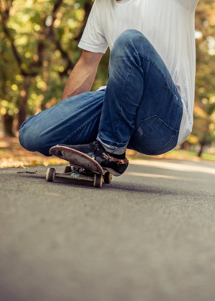 Skateboarder squatting on a skate and ride through the forest - Foto, afbeelding