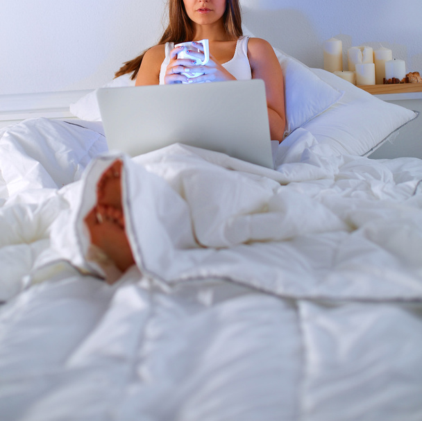Young woman with laptop in bed and enjoying a cup of tea - Photo, image
