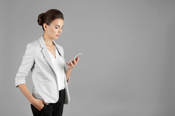 Beautiful businesswoman with phone on gray background - Foto, Imagen