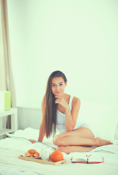 Young beautiful woman sitting in bed and writing in a copybook - Fotoğraf, Görsel