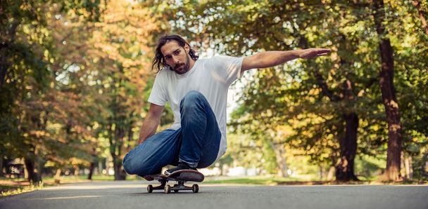 Skateboarder squatting on a skate and ride through the forest - 写真・画像