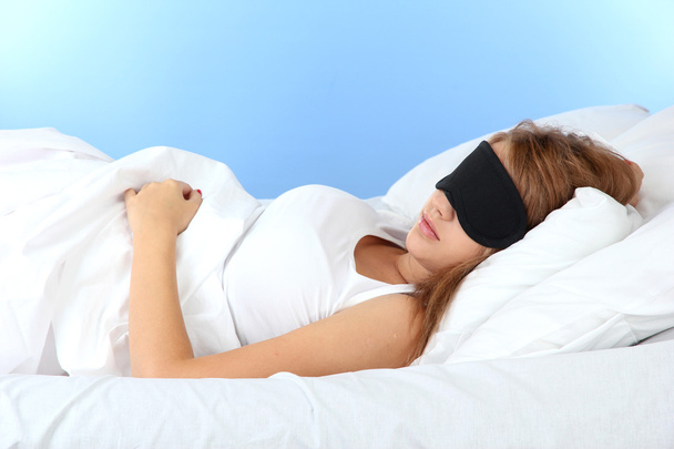 young beautiful woman sleeping in bed with eye mask on blue background - Foto, imagen