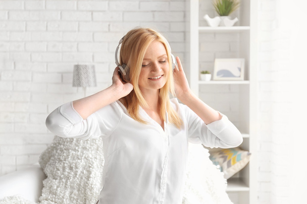 Young woman with headphones listening to music and having fun in a light room - Φωτογραφία, εικόνα