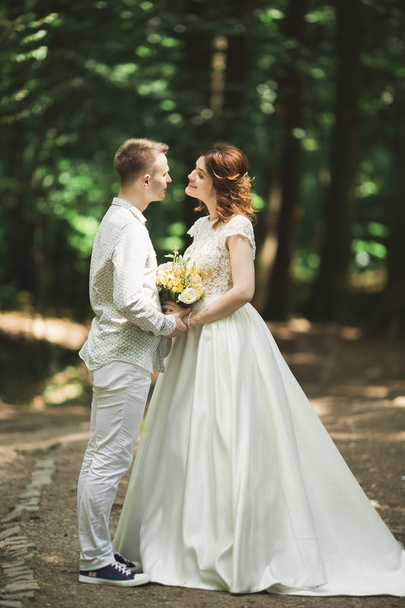 Stylish couple of happy newlyweds walking in the park on their wedding day with bouquet - 写真・画像