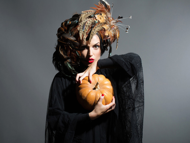 pretty woman in feather hat holds halloween pumpkin - Фото, изображение