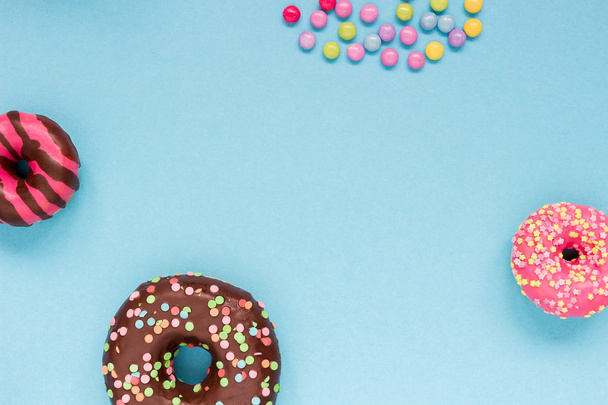 Γλυκό donuts με πολύχρωμες καραμέλες στο μπλε φόντο. - Φωτογραφία, εικόνα