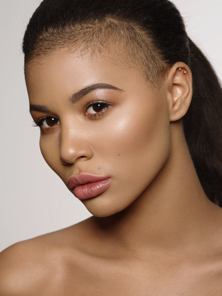 Fashion portrait of an extraordinary beautiful african american young woman with perfect smooth golden skin, full lips and shaved haircut, studio shoot, light background - Foto, afbeelding