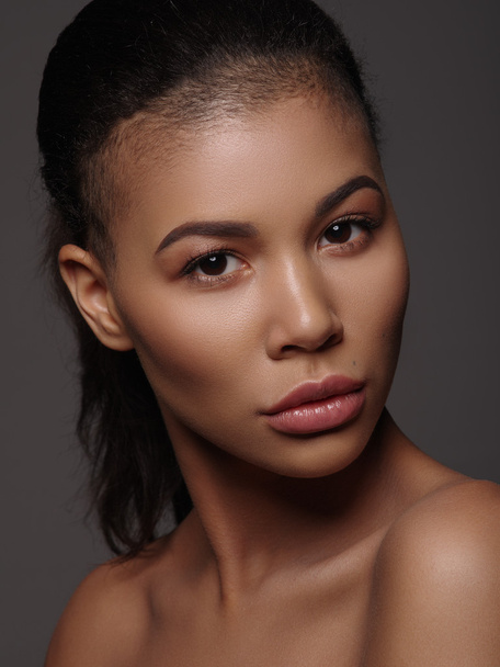 Fashion portrait of an extraordinary beautiful african american young woman with perfect smooth golden skin, full lips and shaved haircut, studio shoot, dark background - Zdjęcie, obraz