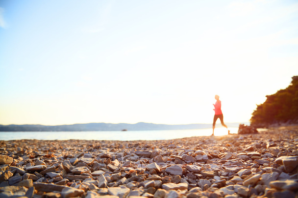Silueta de mujer corriendo en la playa cerca del mar al amanecer
. - Foto, Imagen