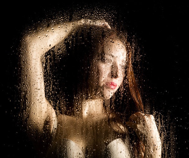 Smooth portrait of sexy model, posing behind transparent glass covered by water drops. - Fotó, kép