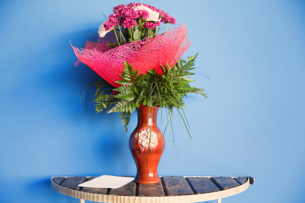 Квітковий букет у глиняній вазі на столі на синій дерев'яній стіні backgro
 - Фото, зображення