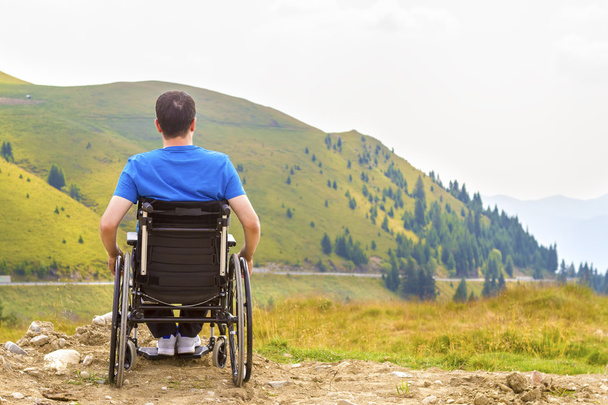 Νεαρός άνδρας σε μια αναπηρική καρέκλα απολαμβάνοντας φρέσκο αέρα σε μια ηλιόλουστη μέρα - Φωτογραφία, εικόνα