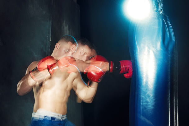 Male boxer boxing in punching bag with dramatic edgy lighting in a dark studio - Foto, imagen
