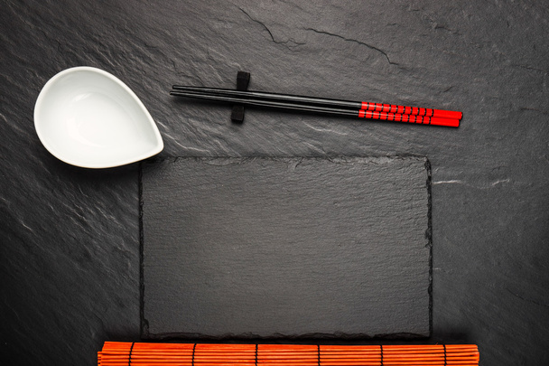 Two chopsticks and white bowl on black stone background with copyspace, top view - Фото, изображение