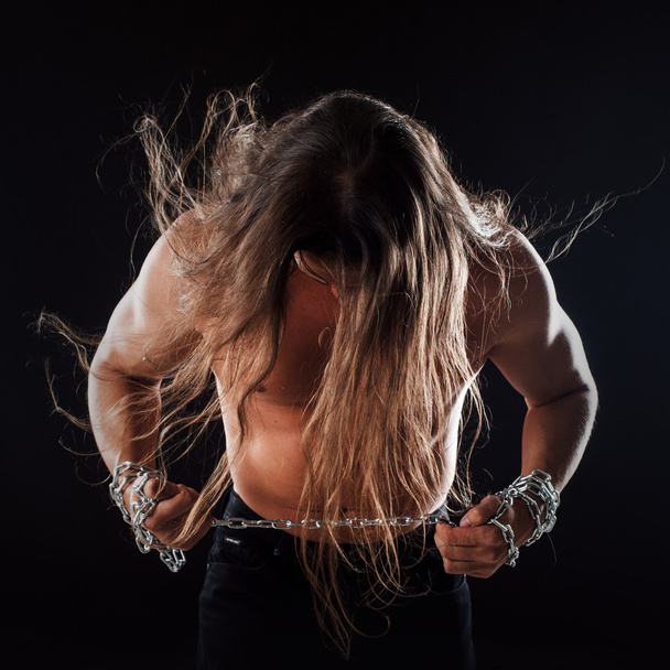 Young man with long hair breaks the iron chain, leaned forward. Strong. Concept of resistance - Foto, imagen