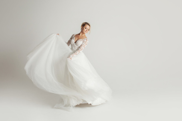 Beautiful attractive bride in wedding dress with long full skirt, white background, dance and smile - Foto, imagen