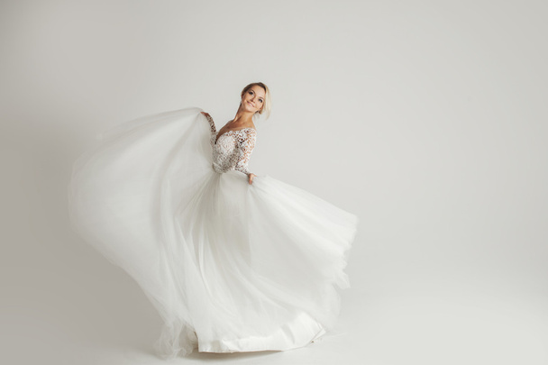 Beautiful attractive bride in wedding dress with long full skirt, white background, dance and smile - Φωτογραφία, εικόνα