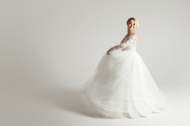 Beautiful attractive bride in wedding dress with long full skirt, white background, dance and smile - Valokuva, kuva
