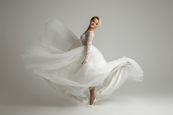 Beautiful attractive bride in wedding dress with long full skirt, white background, dance and smile - Foto, imagen