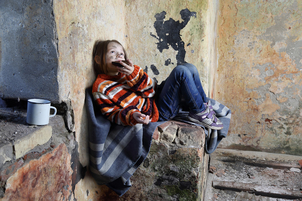 Mała dziewczynka siedzi w piwnicy i zjeść kawałek chleba - Zdjęcie, obraz