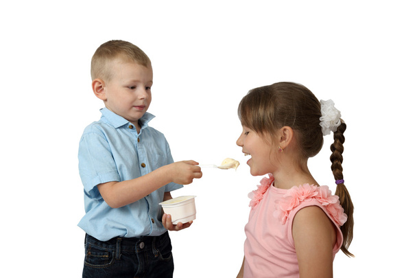 Мальчик кормит девочку за йогуртом ложкой, фокусируясь на девушке и спо.
 - Фото, изображение