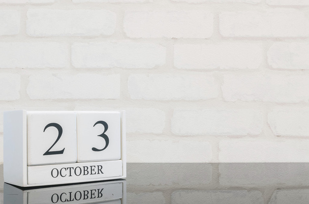 Gros plan calendrier en bois blanc avec mot noir 23 octobre sur table en verre noir et mur de briques blanches fond texturé avec espace de copie, mise au point sélective au calendrier
 - Photo, image