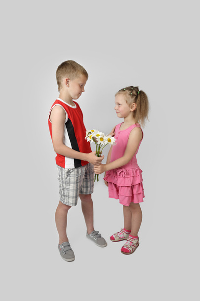 Boy gives girl bouquet of daisies on gray - Photo, Image