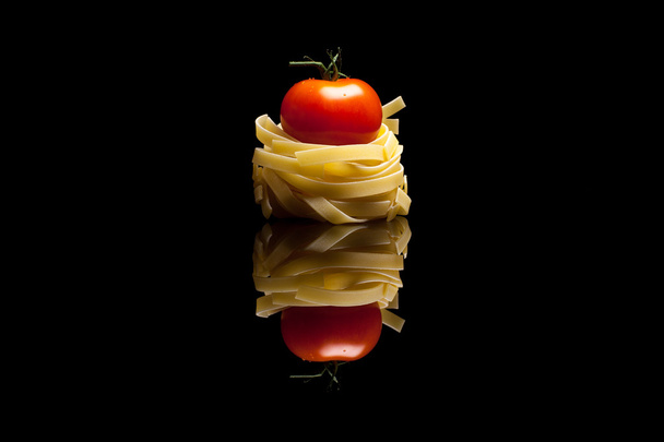 Nest pasta with red tomato black reflective background - Photo, Image