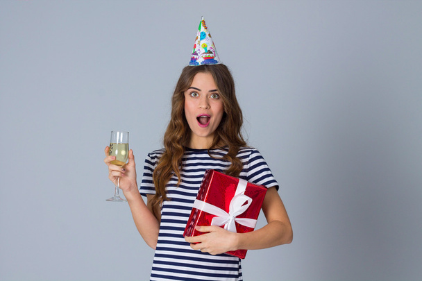 Woman in celebration cap holding a present and a glass - Foto, afbeelding