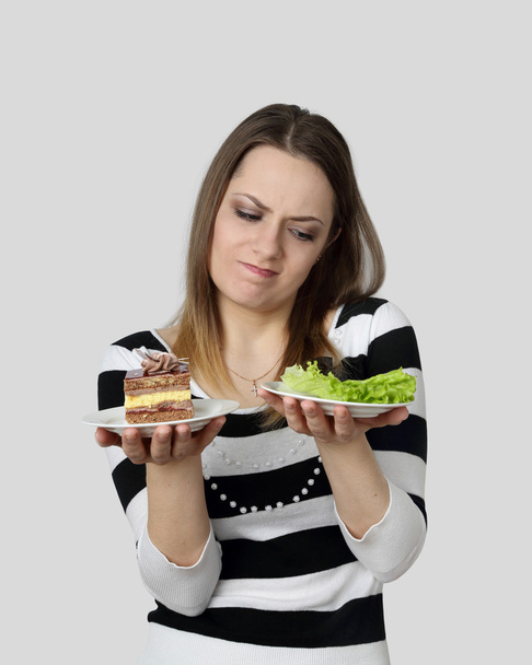 Young woman makes choise between cake and lettuce - Photo, Image