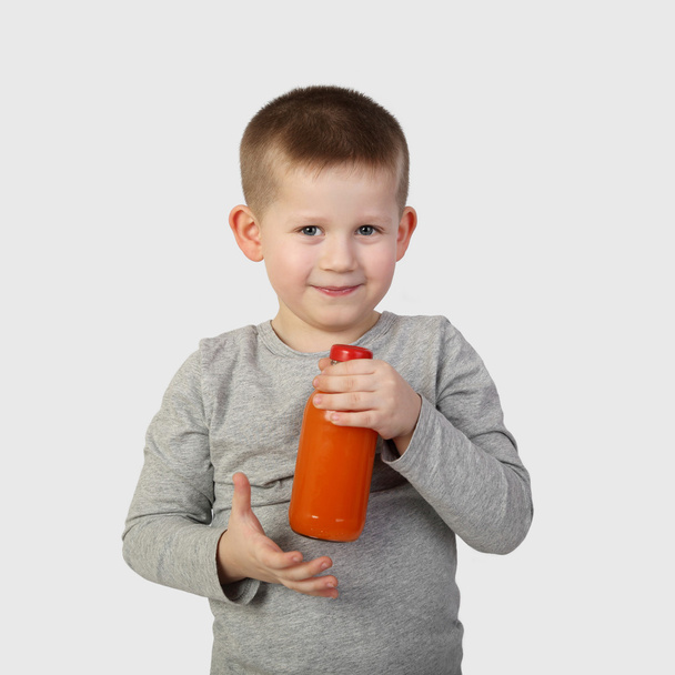 Niño pequeño con botella de jugo de zanahoria naranja en la mano
 - Foto, Imagen
