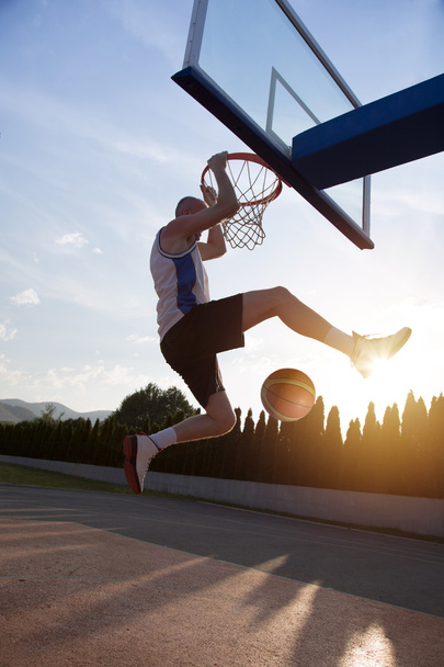 Young man jumping and making a fantastic slam dunk playing stree - Foto, afbeelding