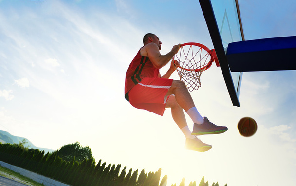 Young basketball player drives to the hoop for a high flying slam dunk in front of sunset sky. - Foto, Bild