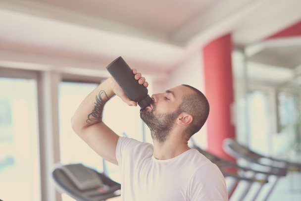 Young adult man drinking bottle of water on trreadmill in gym. - Fotó, kép