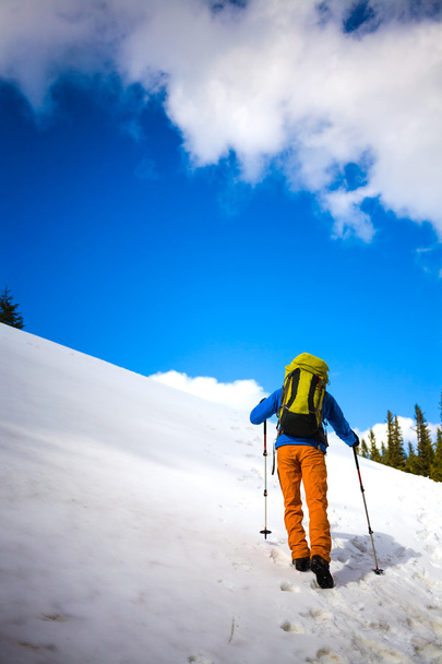 Ορειβάτης βουνών περπατά σε μια χιονισμένη πλαγιά. - Φωτογραφία, εικόνα