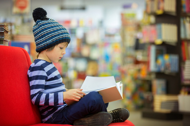 Adorable little child, boy, sitting in a book store - Фото, изображение