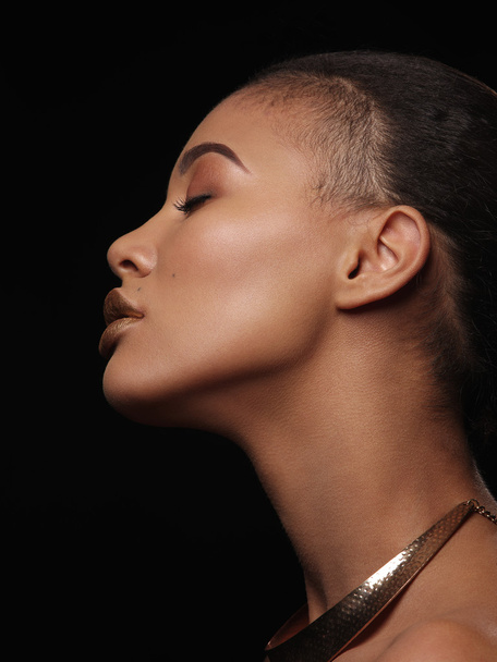 Fashion studio portrait of an extraordinary beautiful nude african american woman with perfect smooth glowing mulatto skin, make up, full golden lips, shaved haircut and gold necklace, profile - 写真・画像