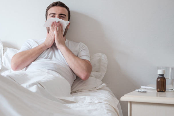 Man feeling cold, lying in the bed and blowing his nose - Photo, Image