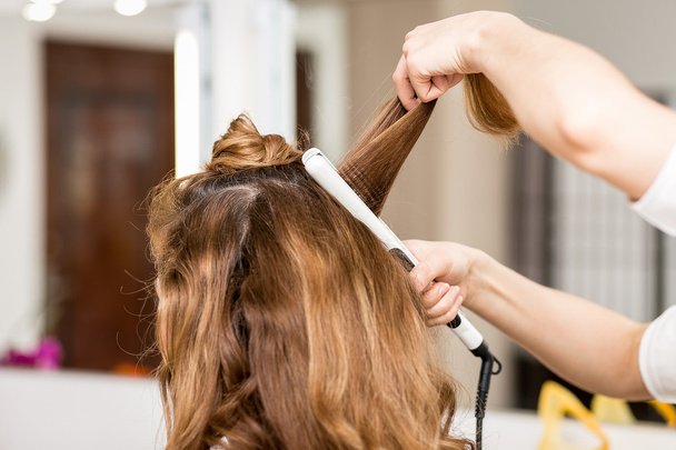Professional hairdresser using curling iron. Hair curls in beauty salon - Фото, зображення