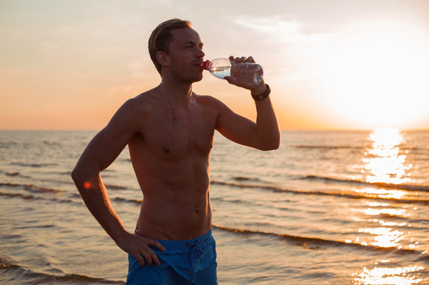 Вмістити чоловіка пити воду на пляжі після тренування
 - Фото, зображення