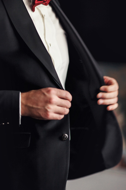 Man with red bow tie buttons up his black blazer - Zdjęcie, obraz