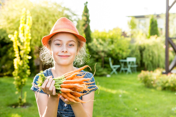 Child girl holding bunch of young carrots in the garden - Foto, imagen