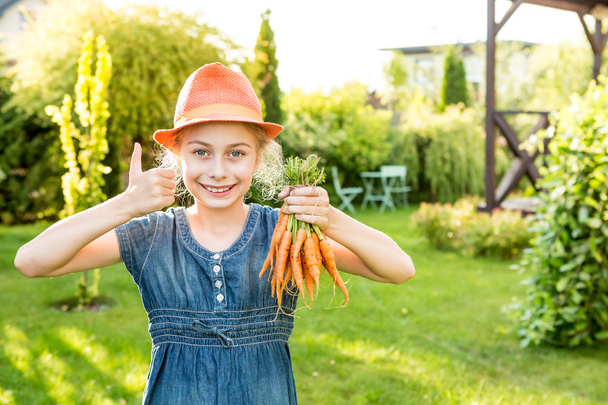 Child girl holding bunch of young carrots in the garden - Foto, imagen