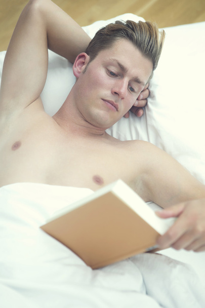 blond man lying in bed and reading a book - Φωτογραφία, εικόνα